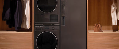 Black Fisher & Paykel washer and dryer set against a wooden wardrobe with clothes and decor items.